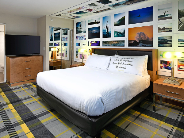 Modern hotel room with a large bed, wall-to-wall photo collage, plaid carpet, wooden furniture, and soft lighting&mdash;cozy, contemporary vibe.