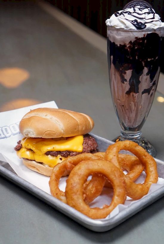 A cheeseburger with melted cheese, onion rings, and a chocolate milkshake sundae topped with whipped cream.
