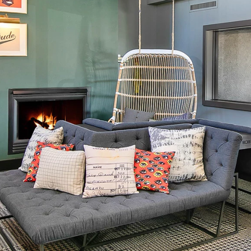 A modern living room with a teal accent wall, a cozy gray sofa, a hanging chair, a fireplace, bookshelves, and decorative cushions neatly arranged.