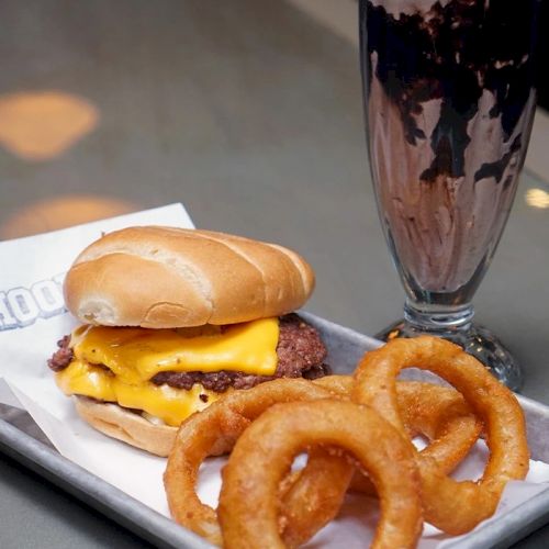 Juicy cheeseburger with melted cheese, a soft bun, crispy onion rings, and a tall chocolate milkshake topped with whipped cream.